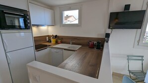 A compact kitchen with a microwave, oven, and dishwasher. There's a small window above the sink and a TV mounted on the wall. - Balcon des îles d'Or - T2 seafront historic center (Le Lavandou)