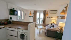 A compact apartment with a kitchen, a washing machine, a sofa, and a dining area. - Balcon des îles d'Or - T2 seafront historic center (Le Lavandou)
