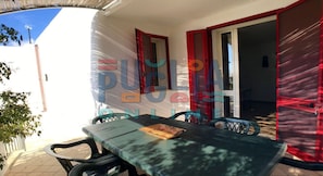 An outdoor patio with a table and chairs, a red-framed door, and a view of the sky.