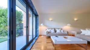 A modern living room with a sofa, coffee table, and floor lamps. Large windows offer a view of the outdoors. - Stunning Modern Apartment [122] (Lagos)