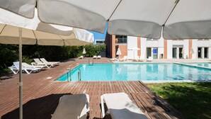 A swimming pool with lounge chairs and umbrellas, surrounded by a wooden deck and a building with a brick facade. - Stunning Modern Apartment [122] (Lagos)