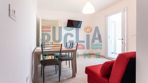Un área de comedor con una mesa y sillas, un televisor montado en la pared, y una silla roja en primer plano.