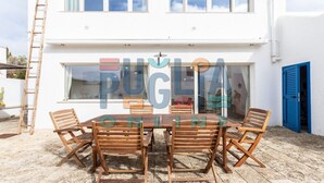 A white building with a large window and a blue door. There is a wooden table and chairs outside. - Villa Pisa 2 in Torre Vado (Torre vado)