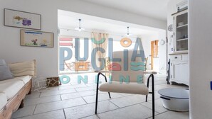 A spacious living room with a sofa, a chair, and a dining area visible through a glass door. - Villa Pisa 2 in Torre Vado (Torre vado)