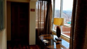 A hotel room with a wooden floor, a dining table with chairs, a lamp, and a view of a cityscape through large windows. - Zans Apartments Cusco 4 (Cusco)