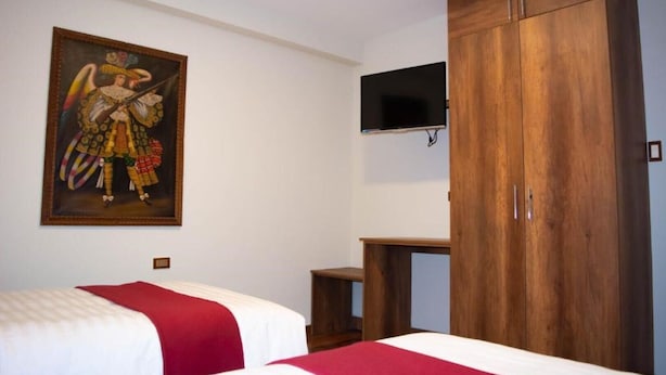 Quarto de hotel com duas camas, um guarda-roupa de madeira, televisão montada e um quadro na parede.