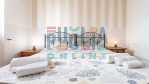 Un lit bien fait, agrémenté d’une couvre-lit aux motifs tropicaux, d’une tête de lit en métal et de deux tables de chevet avec des lampes.