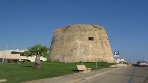 Une tour de pierre historique, avec un espace verdoyant devant, un palmier et un panneau indiquant un parking.