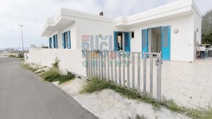 Un bâtiment moderne de couleur blanche, doté de volets bleus, d’une entrée fermée par un portail et d’un chemin piétonnier dallé.