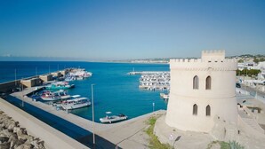 Un port de plaisance sur la côte, avec des bateaux amarrés, une tour et un ciel bleu dégagé.