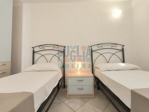 Een slaapkamer met twee enkele bedden, een nachtkastje met een lamp en een kleine ladekast.