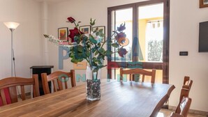 Zona pranzo con tavolo in legno, sedie, un vaso con fiori e quadri appesi al muro.