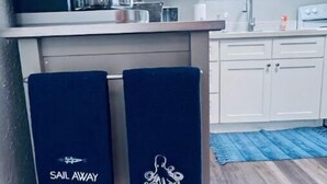 A kitchen with white cabinets, a coffee machine, and two towels hanging on the oven with a nautical design. - Makin’ Waves Cottage- 4 min. to Cruise Ports and half mile from beach (Galveston)