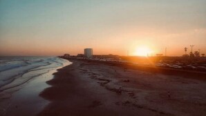 A beach with a sunset, a pier, and a tall building. - Makin’ Waves Cottage- 4 min. to Cruise Ports and half mile from beach (Galveston)