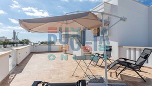 A rooftop terrace with a large umbrella, outdoor seating, and a view of the city skyline. - Apartment Gioia 1 in Marina di Pescoluse (Torre Vado)
