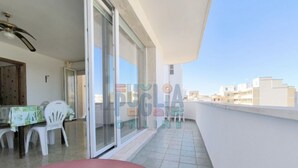 Een balkon met een tafel, stoelen, een schuifpui en uitzicht op gebouwen.