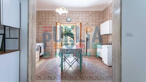 A narrow hallway leading to a dining area with a patterned floor, a table with a colorful tablecloth, and a view of the outside through a glass door. - Villa Lungomare Galilei on the waterfront in Gallipoli (Gallipoli)
