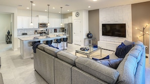 A modern kitchen with white cabinets, a central island with bar stools, and a dining area with a glass table and chairs. - Lovely House 5Beds-4Bath-Private Pool-Club Free (KISSIMMEE)