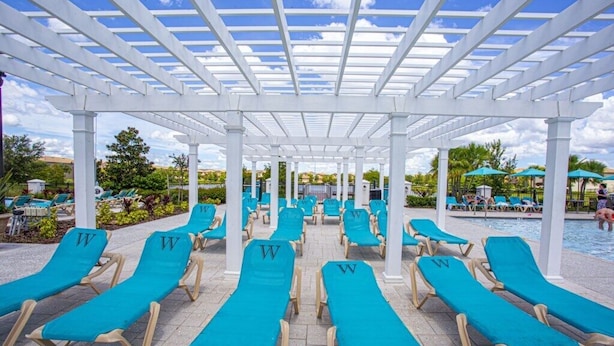 A covered pool area with rows of blue lounge chairs and a white pergola structure. - Lovely House 5Beds-4Bath-Private Pool-Club Free (KISSIMMEE)