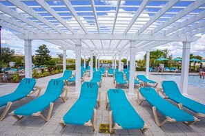 Ein Poolbereich mit Überdachung, Reihen von blauen Liegestühlen und einer weißen Pergola.