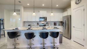 A modern kitchen with white cabinets, stainless steel appliances, a marble island, and black bar stools. - Lovely House 5Beds-4Bath-Private Pool-Club Free (KISSIMMEE)