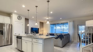 A modern kitchen with a central island, built-in appliances, pendant lighting, and a large window providing natural light. - Lovely House 5Beds-4Bath-Private Pool-Club Free (KISSIMMEE)
