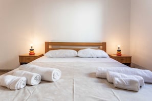 Ein ordentlich gemachtes Bett mit weißen Leinen und Kissen, zwei Nachttische mit Lampen und aufgerollte Handtücher auf dem Bett.