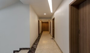 A hallway with a marble floor, wooden doors, and a light fixture on the ceiling. - Treebo Hiland Suites (Bengaluru)