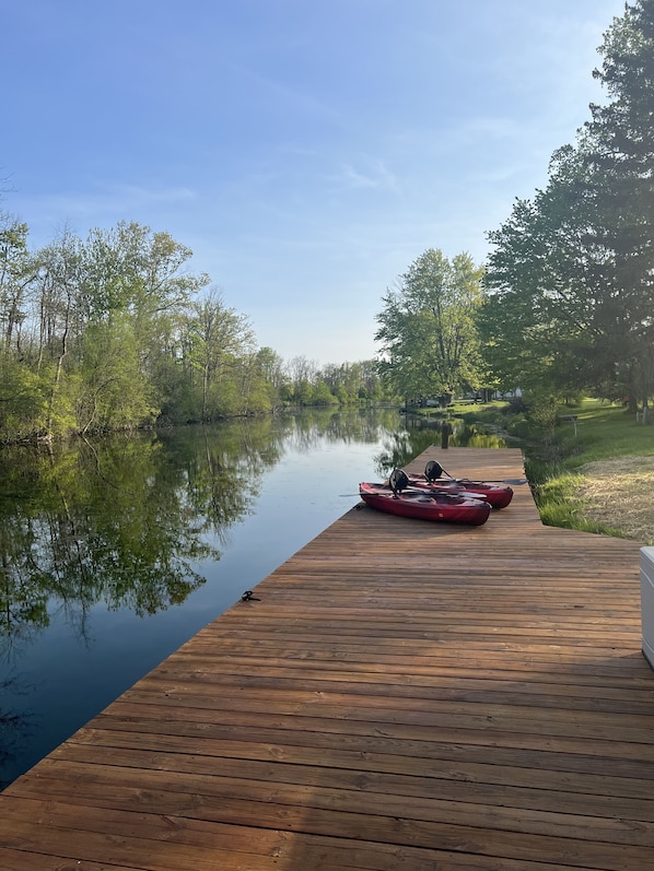 A wooden dock extending into calm water, with kayaks docked at the end.