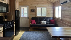 A cabin interior with a kitchen, a dining area, and a seating area with a couch and pillows.