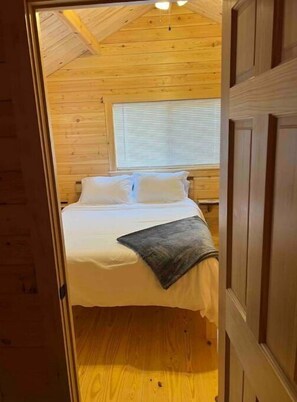 A wooden-paneled bedroom with a bed, pillows, and a blanket. - NEW! Rivers Edge Cabin (Waterloo)