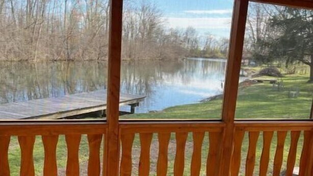 A wooden deck with a railing overlooking a calm lake and grassy area.