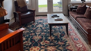 Ein Wohnzimmer mit Deckenventilator, Ledersessel, Sofa, Couchtisch und einem gemusterten Teppich.