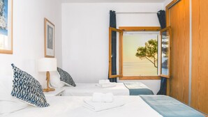 A hotel room with two beds, a window with a view of the sea, and a wooden wardrobe.