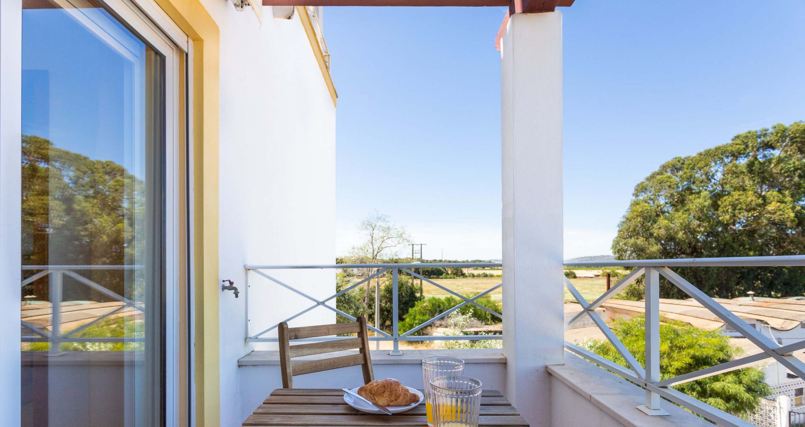 Un balcone con un tavolo, un piatto con un croissant e un bicchiere di succo di frutta.