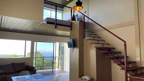 A spacious living area with a wooden dining table, a sofa, and a staircase leading to an upper level. - Loft & Jacuzzi Great View VG Poás (Poás)
