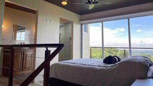 A bedroom with a bed, a ceiling fan, a view of the outdoors, and a kitchen area. - Loft & Jacuzzi Great View VG Poás (Poás)