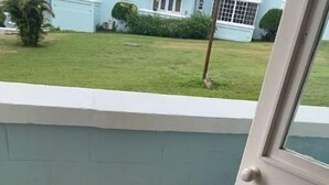 Een klein balkon met een betegelde vloer, een witte deur en uitzicht op een huis met een groen gazon.