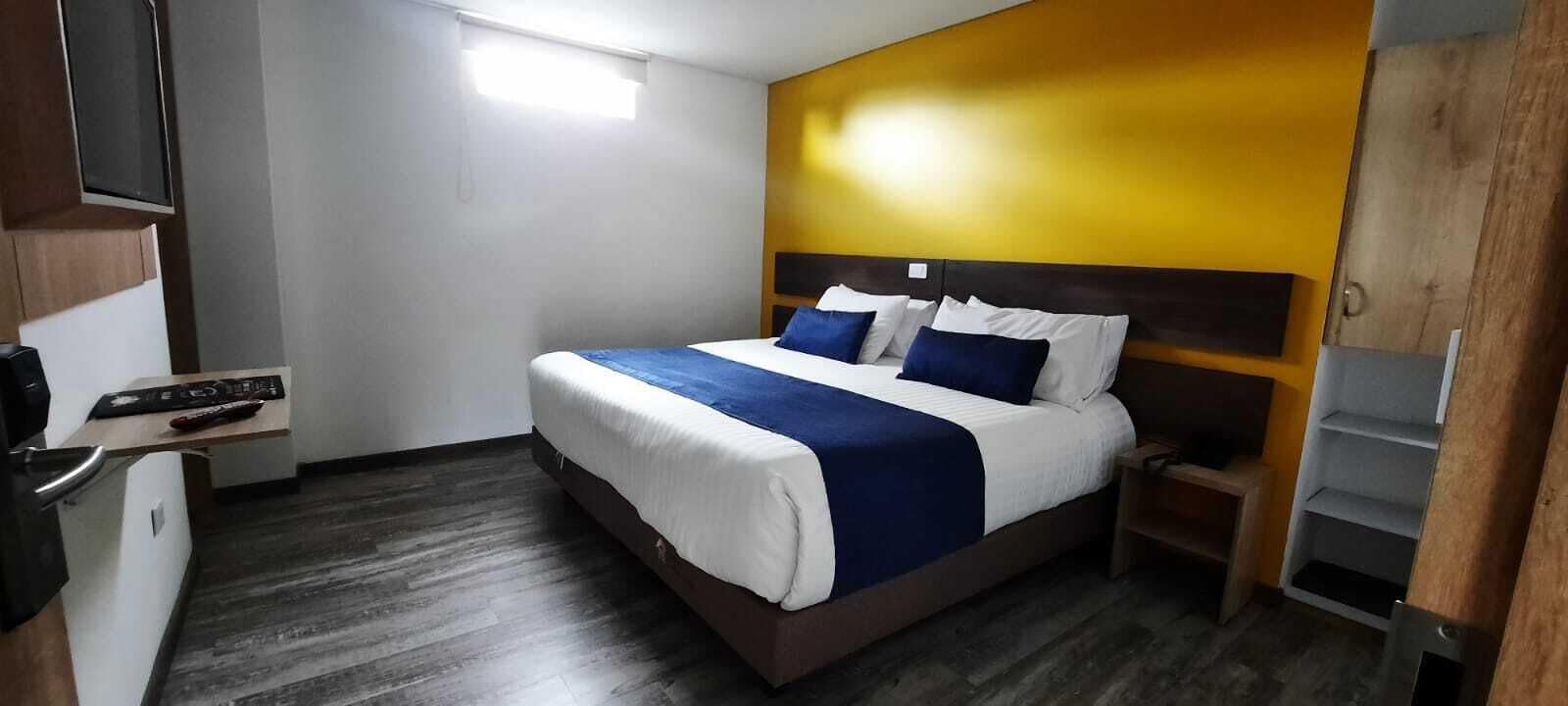 Una habitación de hotel con una cama, televisión, armario de madera y estantería.