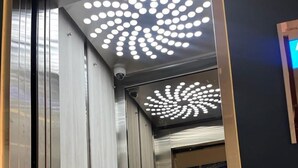 An elevator interior with metallic walls, a glass door, and a ceiling with circular lights. - HOTEL EXPO INN AGORA  (Bogotá)