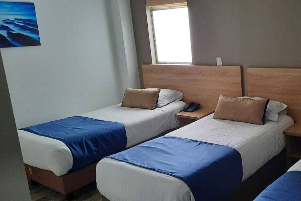 Une chambre d’hôtel avec deux lits simples, chacun doté d’une tête de lit en bois, de draps blancs et d’une touche de couleur bleue.