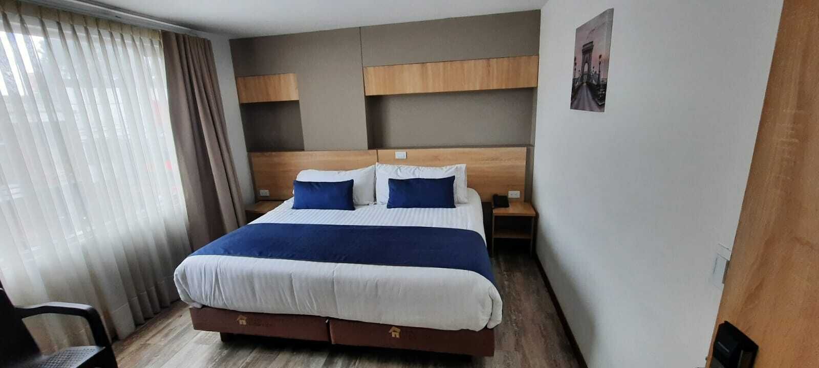 Hotellihuone, jossa on suuri sänky, kaksi yöpöytää, puinen pääty ja ikkuna, jossa on verhot.