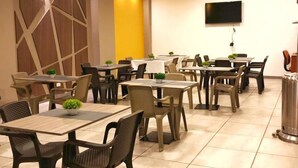 A dining area with multiple tables and chairs, a flat-screen TV mounted on the wall, and a trash can. - HOTEL EXPO INN AGORA  (Bogotá)
