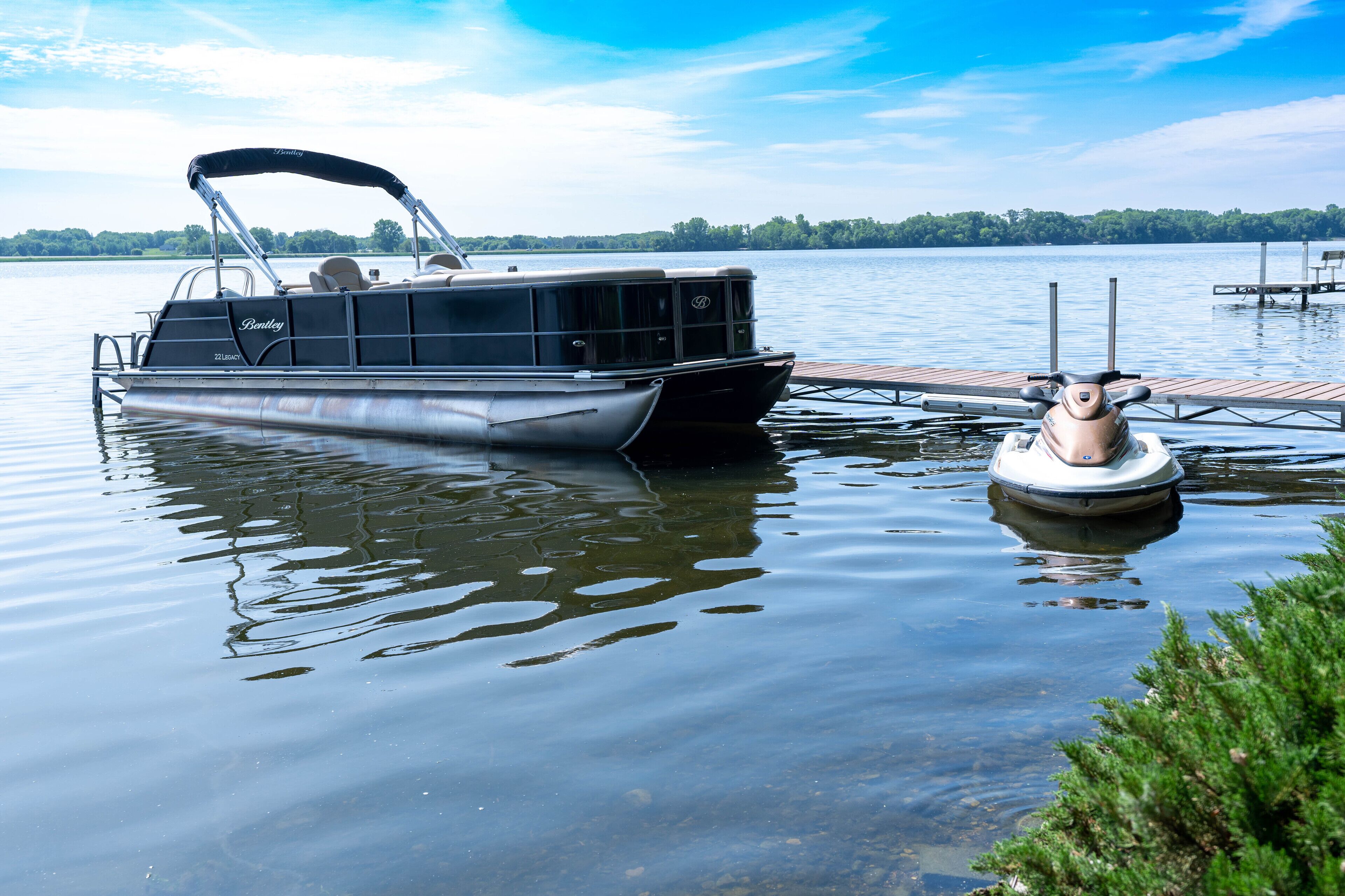 A pontoon boat docked at a wooden pier with a small inflatable boat nearby.