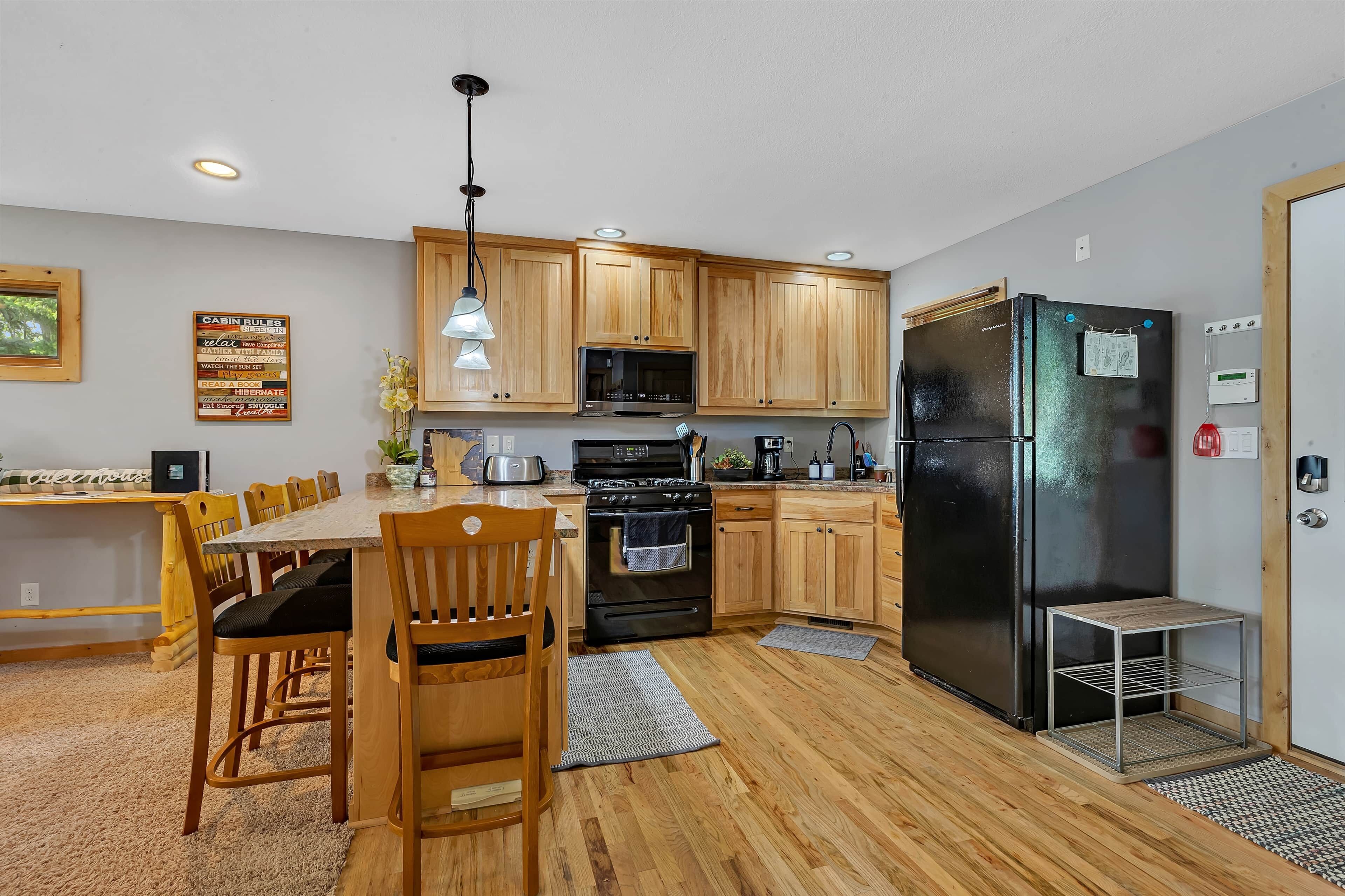 A modern kitchen with wooden cabinets, a black refrigerator, and a dining area with a wooden table and chairs.