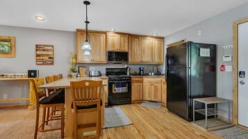 A modern kitchen with wooden cabinets, a black refrigerator, and a dining area with a wooden table and chairs.