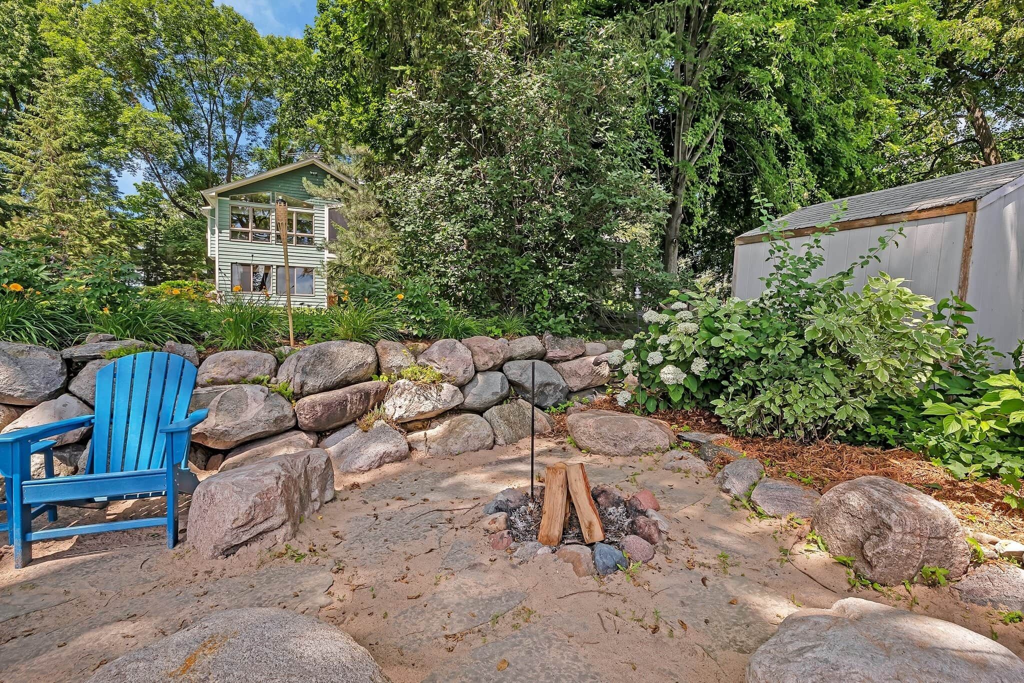 A backyard with a fire pit, a blue Adirondack chair, and a small shed.