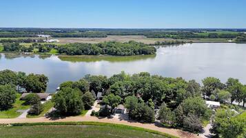 Une propriété située au bord d’un lac, accessible par une route menant à une entrée sécurisée par un portail, et entourée d’une végétation luxuriante et d’une vaste étendue d’eau.