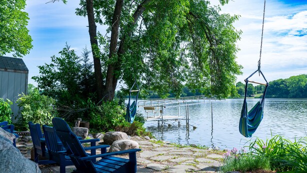 Een terras aan het meer met Adirondack-stoelen, een schommel en een steiger die in het water uitloopt.