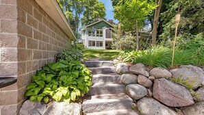 A stone staircase leading to a house with a green roof, surrounded by lush greenery and trees. - Cozy Lakeside Cabin w/ Fireplace & Great Views (Maple Lake Township)